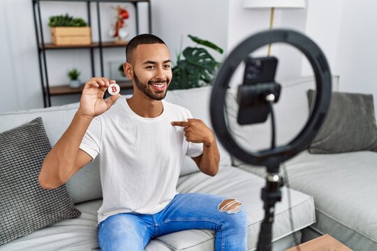 African american man recording vlog tutorial about bitcoin with smartphone at home pointing finger to one self smiling happy and proud