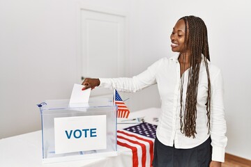 Young african american voter woman putting vote in ballot box at electoral college.