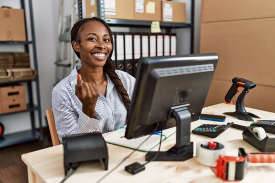 African woman working at small business ecommerce beckoning come here gesture with hand inviting welcoming happy and smiling