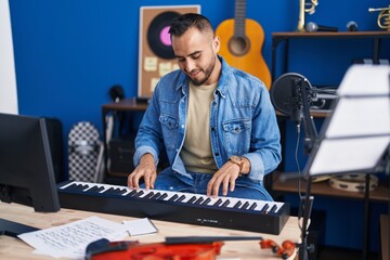 Fototapeta na wymiar Young hispanic man musician playing piano keyboard at music studio