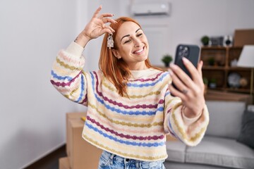 Young caucasian woman having video call holding key at new home