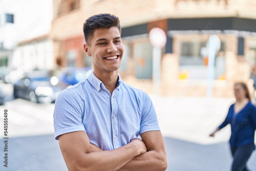 Wall mural young hispanic man smiling confident standing with arms crossed gesture at street