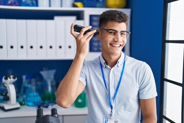 Young hispanic man scientist listening audio message by smartphone working at laboratory