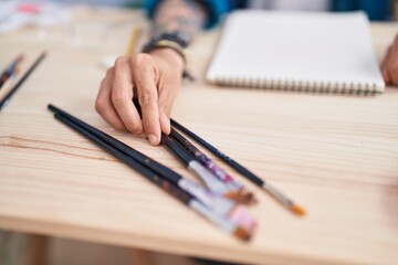 Young hispanic man artist holding paintbrushes at art studio