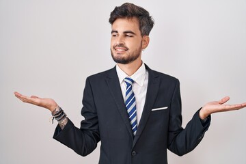 Young hispanic man with tattoos wearing business suit and tie smiling showing both hands open palms, presenting and advertising comparison and balance