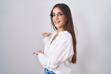 Young brunette woman wearing glasses inviting to enter smiling natural with open hand