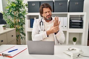 Handsome middle age doctor man working at the clinic suffering pain on hands and fingers, arthritis...
