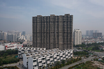 Aerial view of large abandoned concrete shell of residential high-rise real estate and construction development showing town houses and villas with skylline