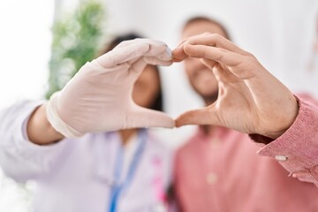 Man and woman doctor and patient doing heart gesture with hands at clinic