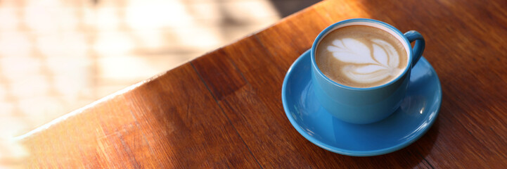 Ceramic cup of aromatic coffee with foam on wooden table in outdoor cafe, space for text. Banner design