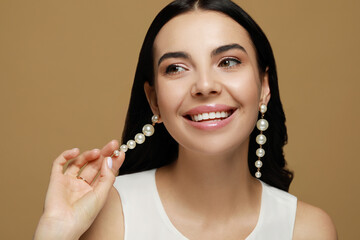 Young woman wearing elegant pearl earrings on brown background