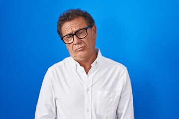 Middle age hispanic man standing over blue background depressed and worry for distress, crying angry and afraid. sad expression.