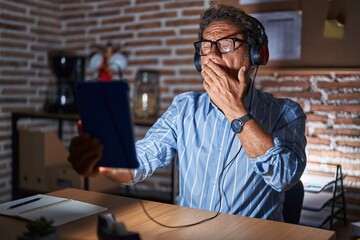 Middle age hispanic man using touchpad sitting on the table at night bored yawning tired covering mouth with hand. restless and sleepiness.