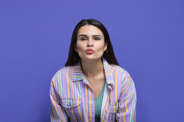 Fototapeta premium Beautiful young woman giving kiss on purple background