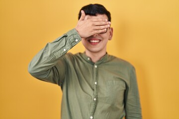 Fototapeta premium Non binary person standing over yellow background smiling and laughing with hand on face covering eyes for surprise. blind concept.