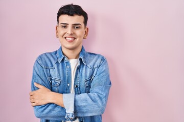 Non binary person standing over pink background happy face smiling with crossed arms looking at the camera. positive person.