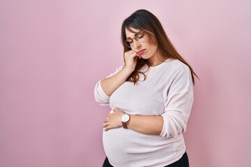 Pregnant woman standing over pink background thinking looking tired and bored with depression...