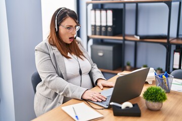 Pregnant woman working at the office wearing operator headset scared and amazed with open mouth for surprise, disbelief face