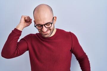 Young bald man with beard standing over white background wearing glasses dancing happy and...
