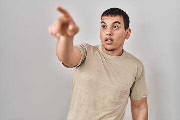 Young arab man wearing casual t shirt pointing with finger surprised ahead, open mouth amazed expression, something on the front
