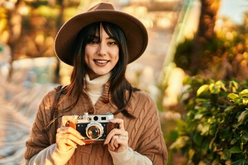 Brunette woman wearing winter hat smiling using vintage camera at the park