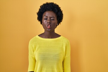 African young woman standing over yellow studio making fish face with lips, crazy and comical gesture. funny expression.