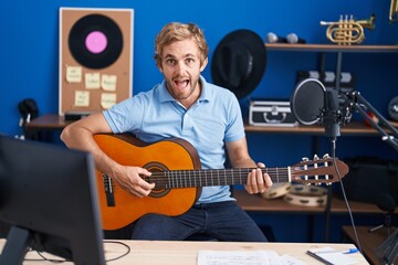 Caucasian man playing classic guitar at music studio smiling and laughing hard out loud because funny crazy joke.
