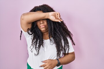 Plus size hispanic woman standing over pink background covering eyes with arm, looking serious and...