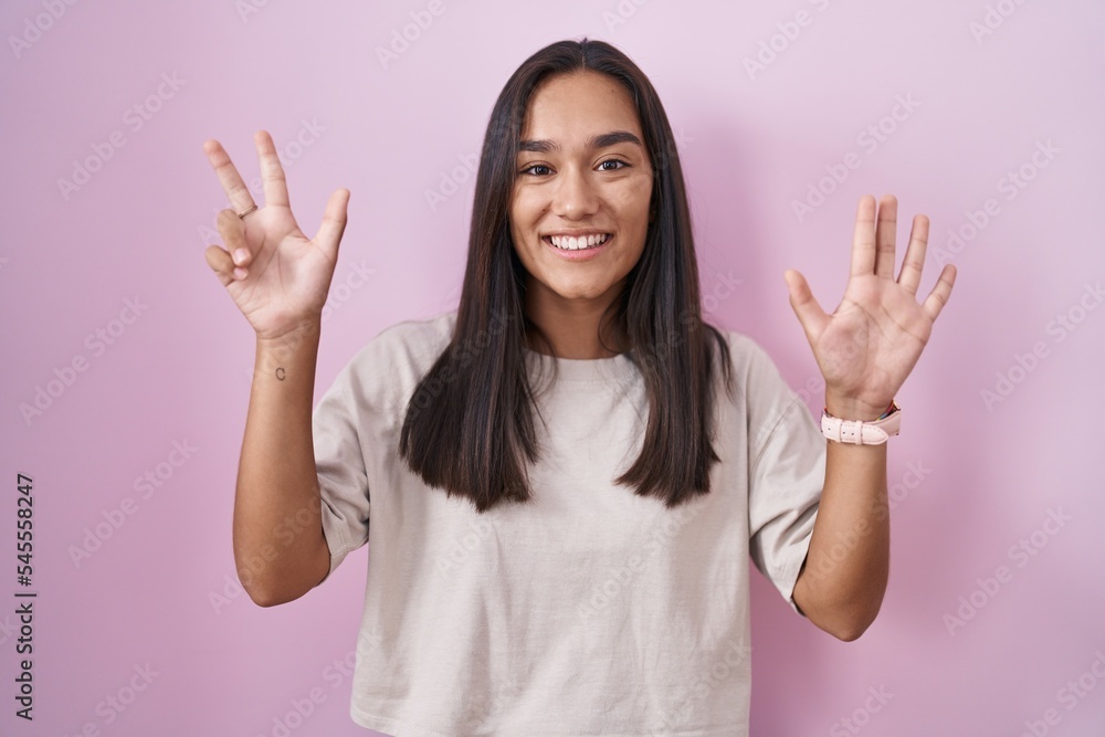 Poster young hispanic woman standing over pink background showing and pointing up with fingers number eight