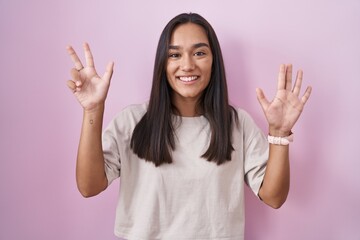 Young hispanic woman standing over pink background showing and pointing up with fingers number eight while smiling confident and happy.