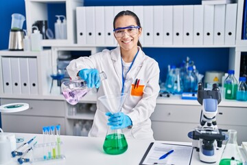 Fototapeta premium Young hispanic woman scientist measuring liquid at laboratory