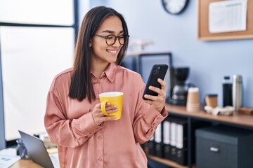 Young hispanic woman business worker using smartphone drinking coffee at office