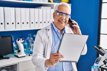 Naklejka na ściany i meble Senior man scientist talking on the smartphone writing on document at laboratory