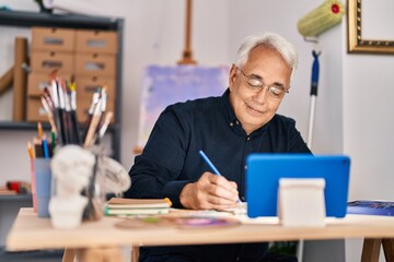 Senior man having online draw lesson sitting on table at art studio