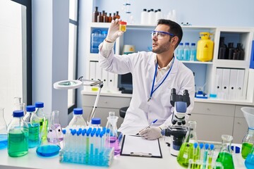 Fototapeta premium Young hispanic man scientist looking urine test tube writing report at laboratory
