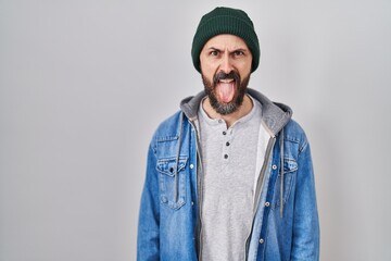 Young hispanic man with tattoos wearing wool cap sticking tongue out happy with funny expression. emotion concept.