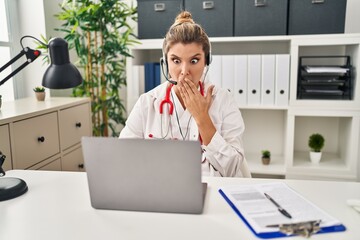 Young doctor woman wearing doctor uniform working using computer laptop covering mouth with hand,...