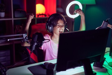 Adorable hispanic girl streamer playing video game with winner expression at gaming room