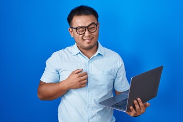 Chinese young man using computer laptop winking looking at the camera with sexy expression,...