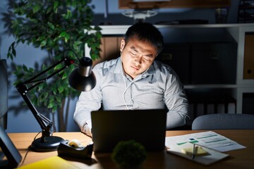 Young chinese man working using computer laptop at night with hand on stomach because nausea, painful disease feeling unwell. ache concept.