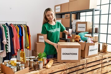 Young chinese woman wearing volunteer uniform packing donations box at charity center