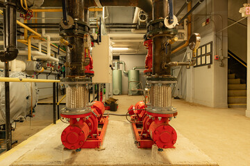 The interior of an old and well used boiler room with two large mechanical pumps, pipes, valves and...