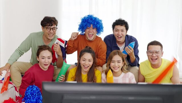 Group of Happy Asian man and woman friends watching world soccer games football competition on television together at home. Sport fans people shouting and celebrating football team victory the match.