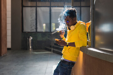 Young black man smoking and using smartphone