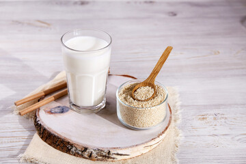 Sesame milk in a glass, sesame seeds in a jar on a wooden background. Healthy vegetarian and vegan drink, plant based milk substitute. 