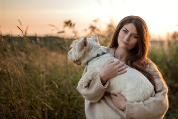 portrait of a beautiful young girl with a dog in her arms, a girl hugs her beloved petam on a walk, West Highland White Terrier, copy space