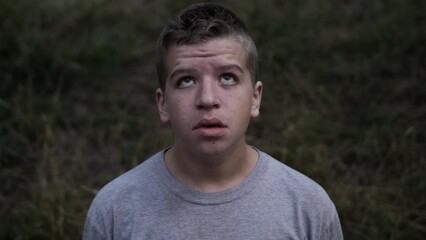 A sad and depressed young teen boy looks up at the sky looking hopeless and afraid