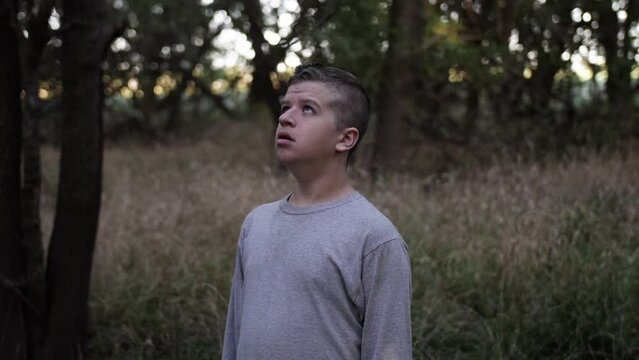A sad, angry young teen boy in the woods looking up at the sky to pray