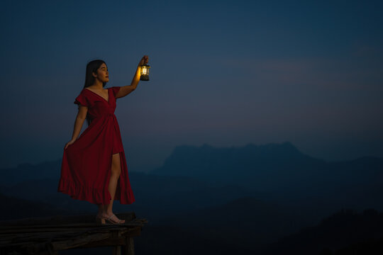 A woman standing with a lantern in the dark night on the mountain.