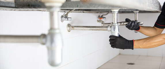 Technician plumber using a wrench to repair a water pipe under the sink. Concept of maintenance, fix water plumbing leaks, replace the kitchen sink drain, cleaning clogged pipes is dirty or rusty.